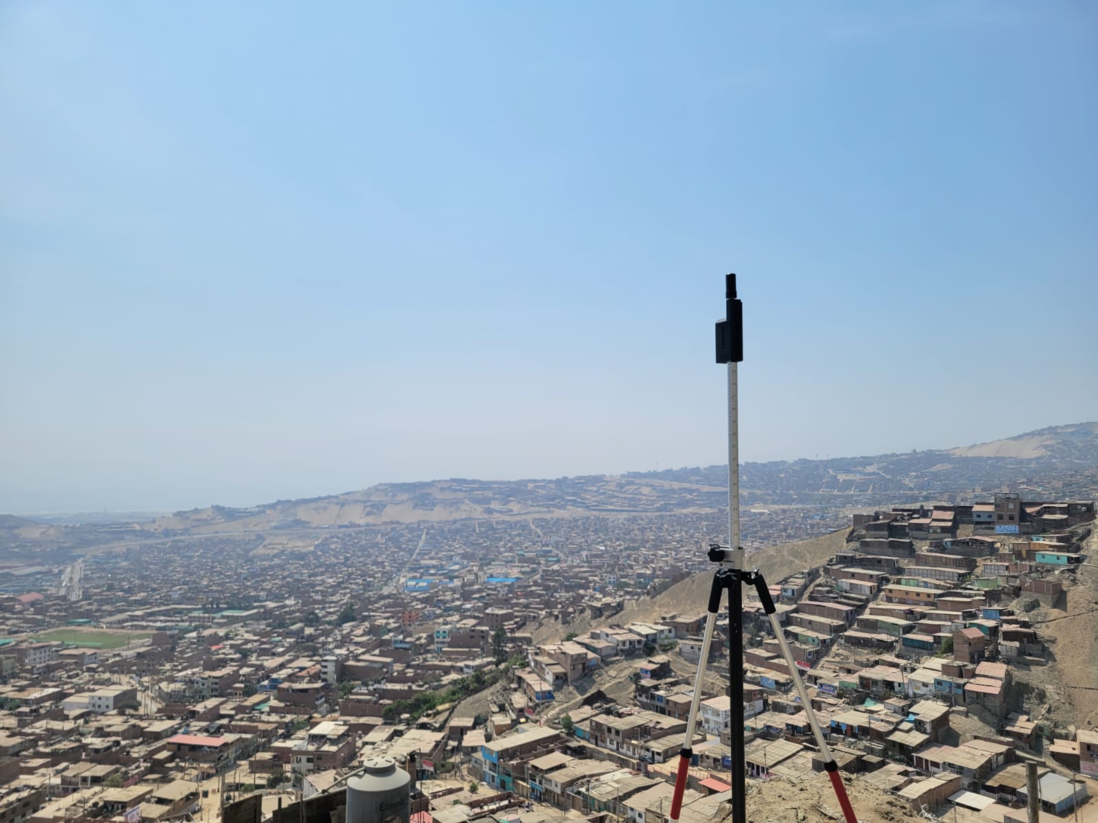Tripod-mounted ROLAVI GNSS receiver overlooking a city